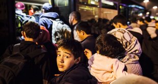 En un puerto de Grecia, un niño y su familia, junto a otros refugiados e inmigrantes, intentan subir a un autobús que los llevará al centro de Atenas. Foto ACNUR/Achilleas Zavallis.